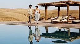 A couple walking around pool at desert camp at sunrise